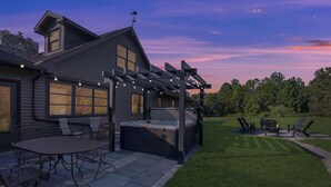 A house with a patio area featuring a hot tub, outdoor seating, and a pergola with string lights.