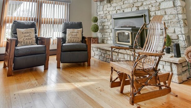 A cozy living room with a stone fireplace, wooden beams, and a ceiling fan.