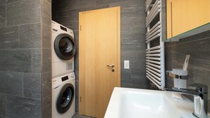 A modern bathroom with a built-in washing machine, a wooden door, a towel rack, and a large sink.