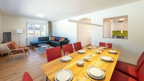 A modern living room with a dining area, featuring a wooden dining table set for six, red chairs, and a sofa in the background.