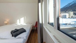 A hotel room with a bed, a chair, a window with a view of a snowy landscape and buildings.