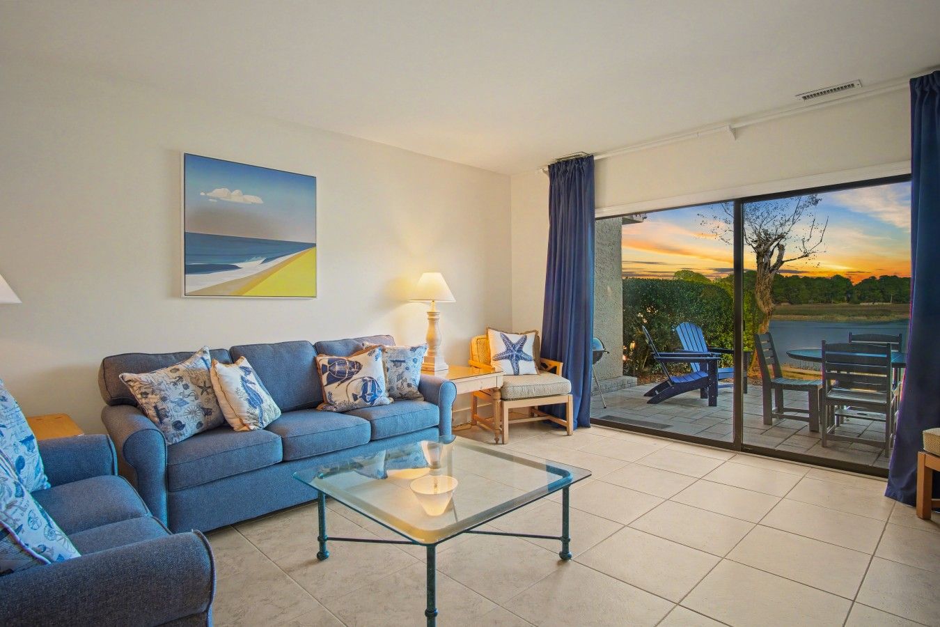 A living room with a sofa, a glass coffee table, and a view of the outdoors through a large sliding glass door.