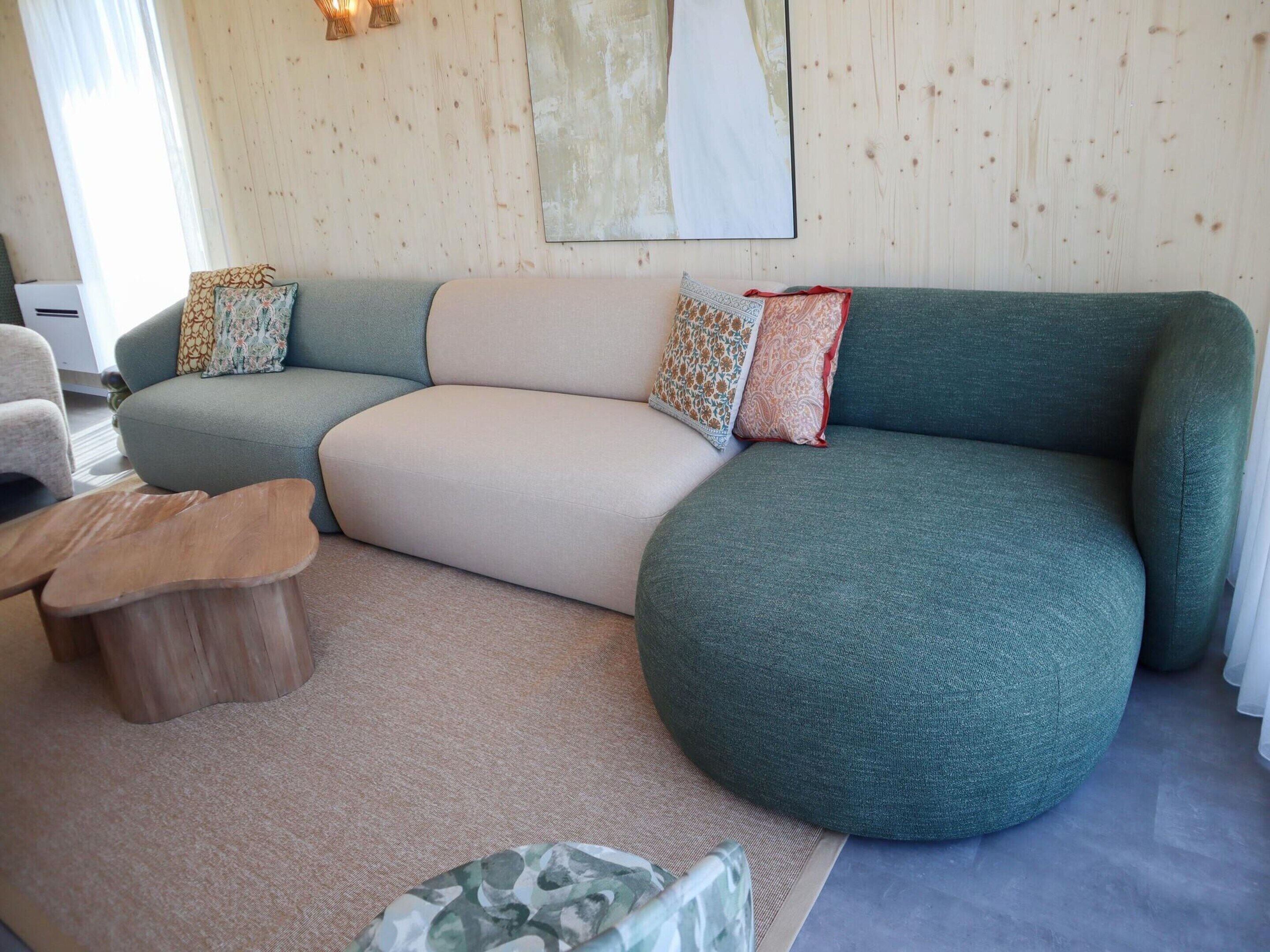 Una sala de estar con un sofá modular, un otoman redondo y una mesa de centro de madera.