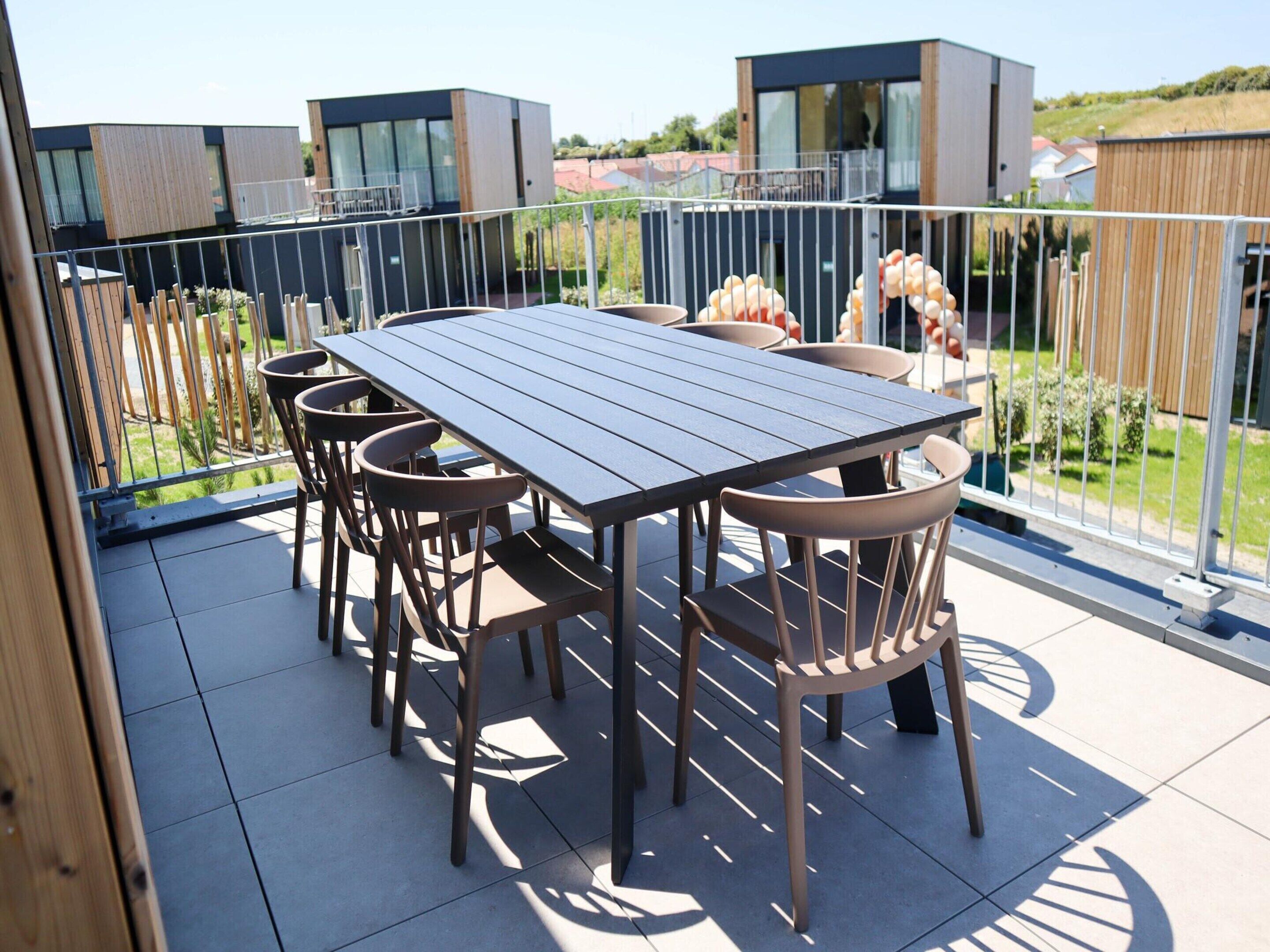 Une terrasse sur le toit, avec une table et des chaises, entourée d’une clôture en métal, d’où l’on a vue sur un quartier résidentiel.
