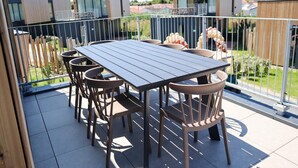 Terraza en la azotea con mesa y sillas, rodeada por una valla metálica, con vistas a una zona residencial.