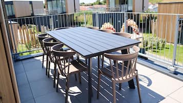 Une terrasse sur le toit, avec une table et des chaises, entourée d’une clôture en métal, d’où l’on a vue sur un quartier résidentiel.