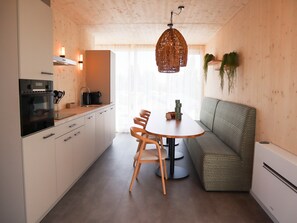 A modern kitchen with a dining table, chairs, and a built-in oven. - Bungalow in Netherlands Near the Coast ('s-Gravenzande)