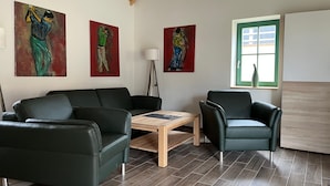 Ein modernes Wohnzimmer mit Holzboden, zwei schwarzen Ledersofas, einem Holztisch und drei abstrakten Bildern an der Wand.