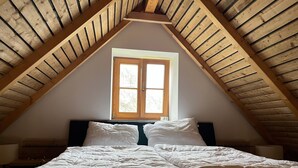 Ein Schlafzimmer mit geneigter Decke, einem Fenster und einem Bett mit weißer Bettwäsche.