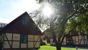Ein traditionelles Fachwerkhäuschen mit sichtbarem Schriftzug "Haus" und "Landliebe" an der Fassade, umgeben von einem gepflegten Rasen und Bäumen.