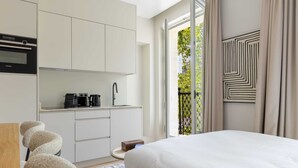 A modern hotel room with a bed, a kitchenette, and a view of greenery through the window. - Marais - Studio in Paris (Paris)