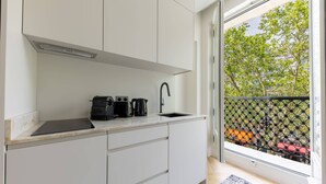 A modern kitchen with white cabinets, a black countertop, and a window with a view of trees and buildings. - Marais - Studio in Paris (Paris)