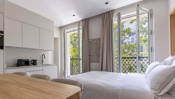 A modern hotel room with a large bed, a wooden dining table, a kitchenette, and a balcony with a view of the city. - Marais - Studio in Paris (Paris)