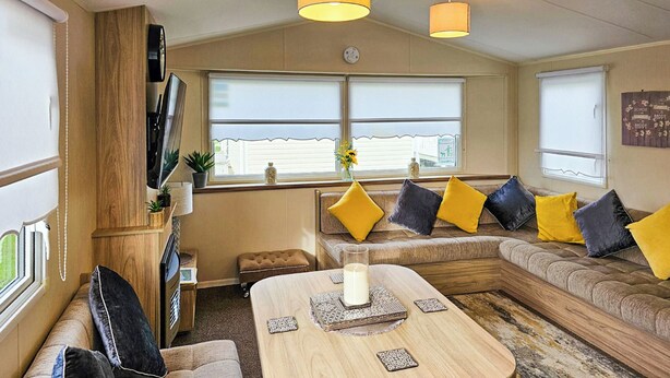 A cozy RV interior with a sofa, a small table, and a TV mounted on the wall. - 3 bedroom accommodation in Rhyl (Rhyl)