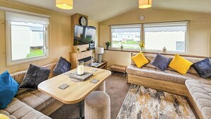 A cozy living room with a sofa, a coffee table, and a TV mounted on the wall. - 3 bedroom accommodation in Rhyl (Rhyl)