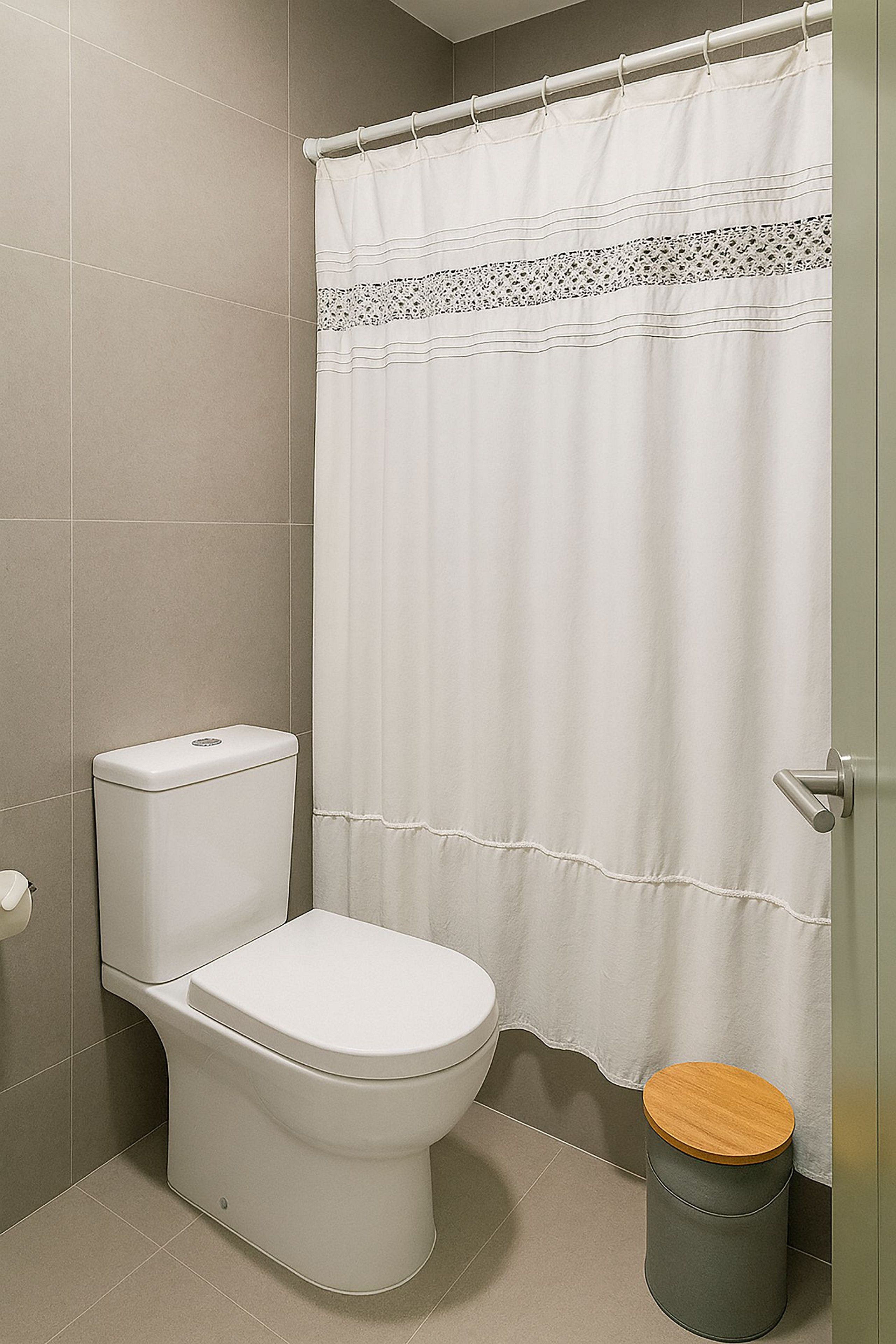 A bathroom with a toilet, a shower curtain, and a trash bin.