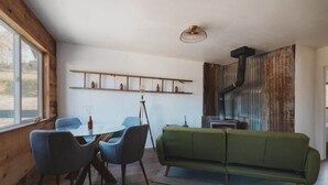 Un interior modern amb zona de menjador, un sofà verd i una paret rústica amb un tub negre.
