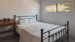 Una camera da letto con un letto singolo, un comodino in legno, una lampada a parete e una finestra vista aperta.