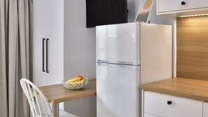 A compact kitchen with white cabinetry, a wooden dining table, and a white chair. - Centro Apartments By Comfortbnb (Sitia)