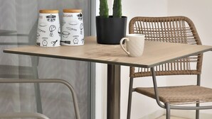 A table with two coffee mugs, a potted cactus, and a wicker chair. - Centro Apartments By Comfortbnb (Sitia)