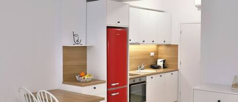 Una habitación de hotel moderna con una cama, un escritorio, un refrigerador rojo, un lavamanos y una pequeña cocina.