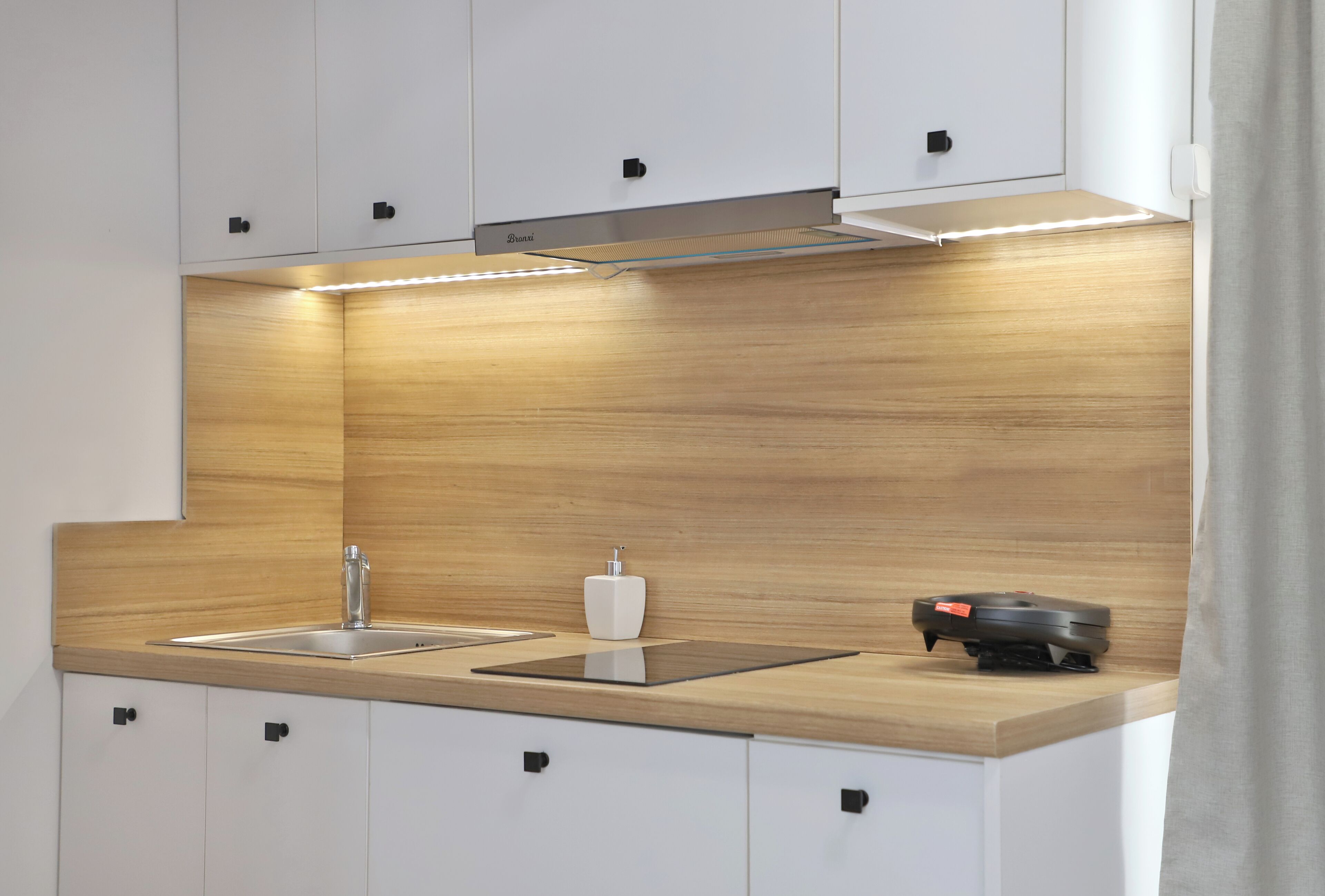 A modern kitchen with white cabinets, a wooden countertop, a stainless steel sink, and a built-in range hood.