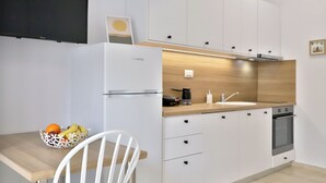 A modern kitchen with white cabinets, a wooden countertop, a built-in oven, and a white chair. - Centro Apartments By Comfortbnb (Sitia)