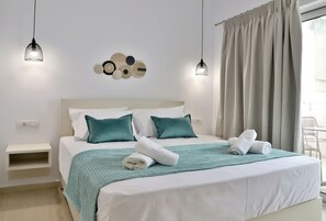 Una cama bien hecha con un edredón color turquesa y dos almohadas, una lámpara fijada a la pared y una ventana con cortinas.