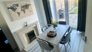 A dining area with a wooden table, chairs, a world map on the wall, a fireplace, and a view of the backyard through large sliding glass doors. - Elegant Escape (Coseley)