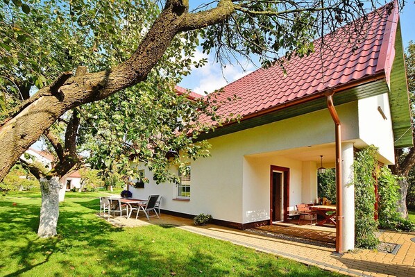 Une maison avec un toit recouvert de tuiles rouges, un patio abrité et une pelouse.