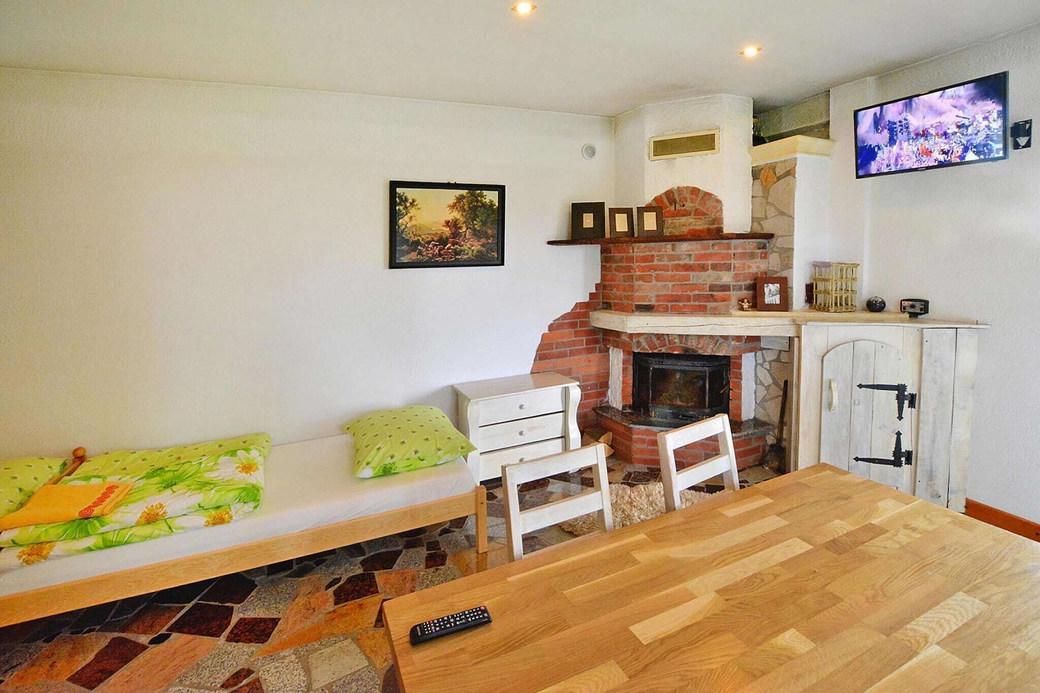 A cozy living room with a fireplace, a television mounted on the wall, a wooden dining table, and a bench with cushions.