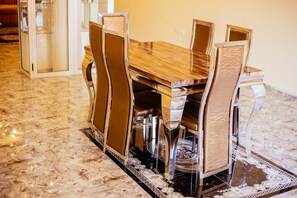 A dining table with chairs, a glass partition, and a patterned rug. - CK Suites (Adentan)
