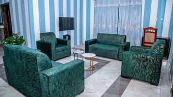 A living room with striped walls, a flat-screen TV, and green upholstered furniture.