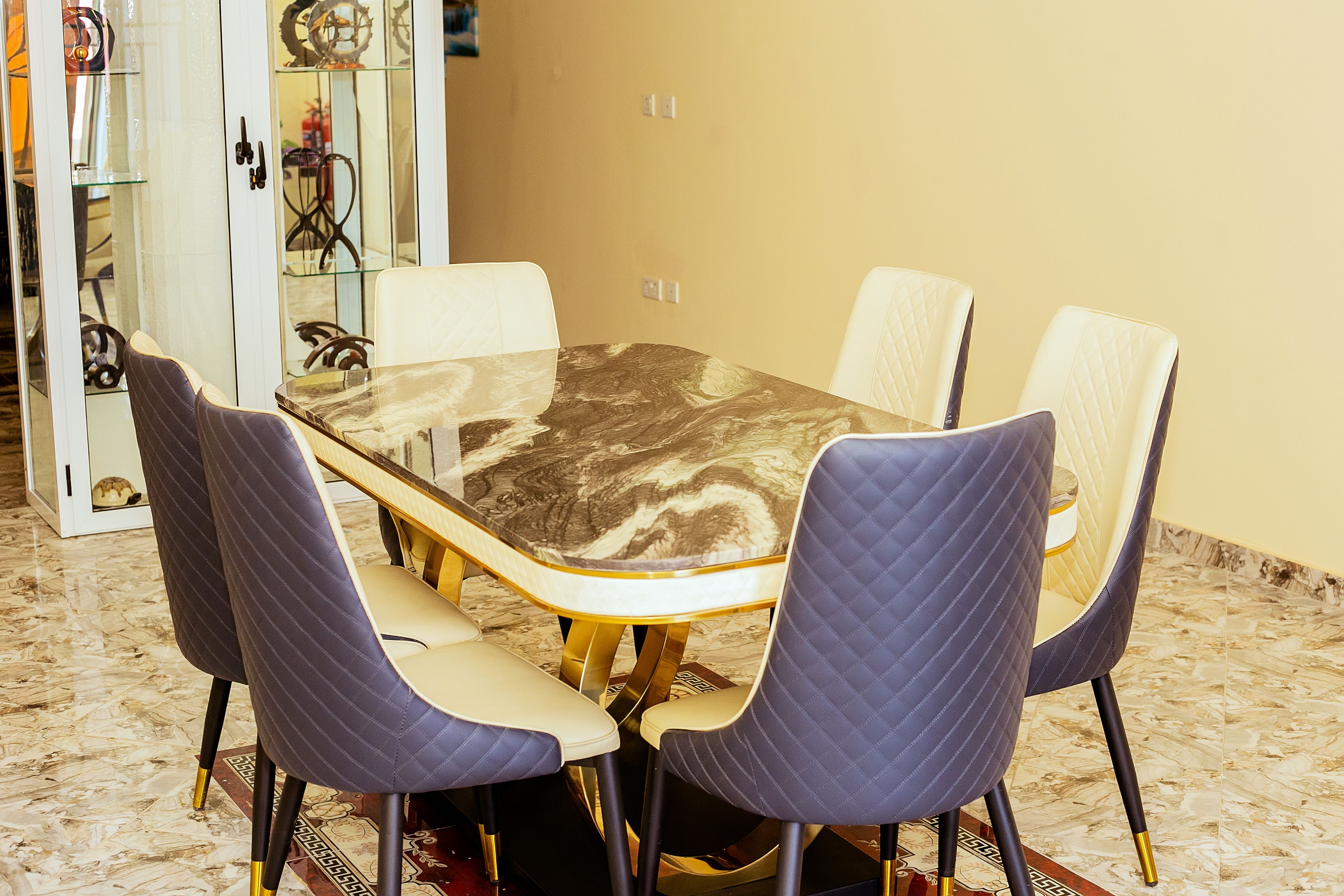 A dining table with a marble top surrounded by four chairs with quilted upholstery.