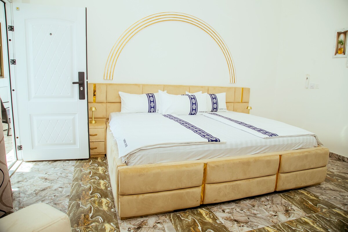 A hotel room with a bed, a nightstand, a door, and a marble-patterned floor.