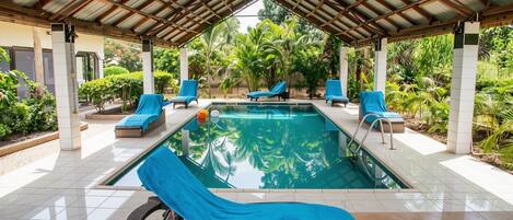 Un espace piscine couvert, doté de chaises longues et offrant une vue sur la végétation tropicale.