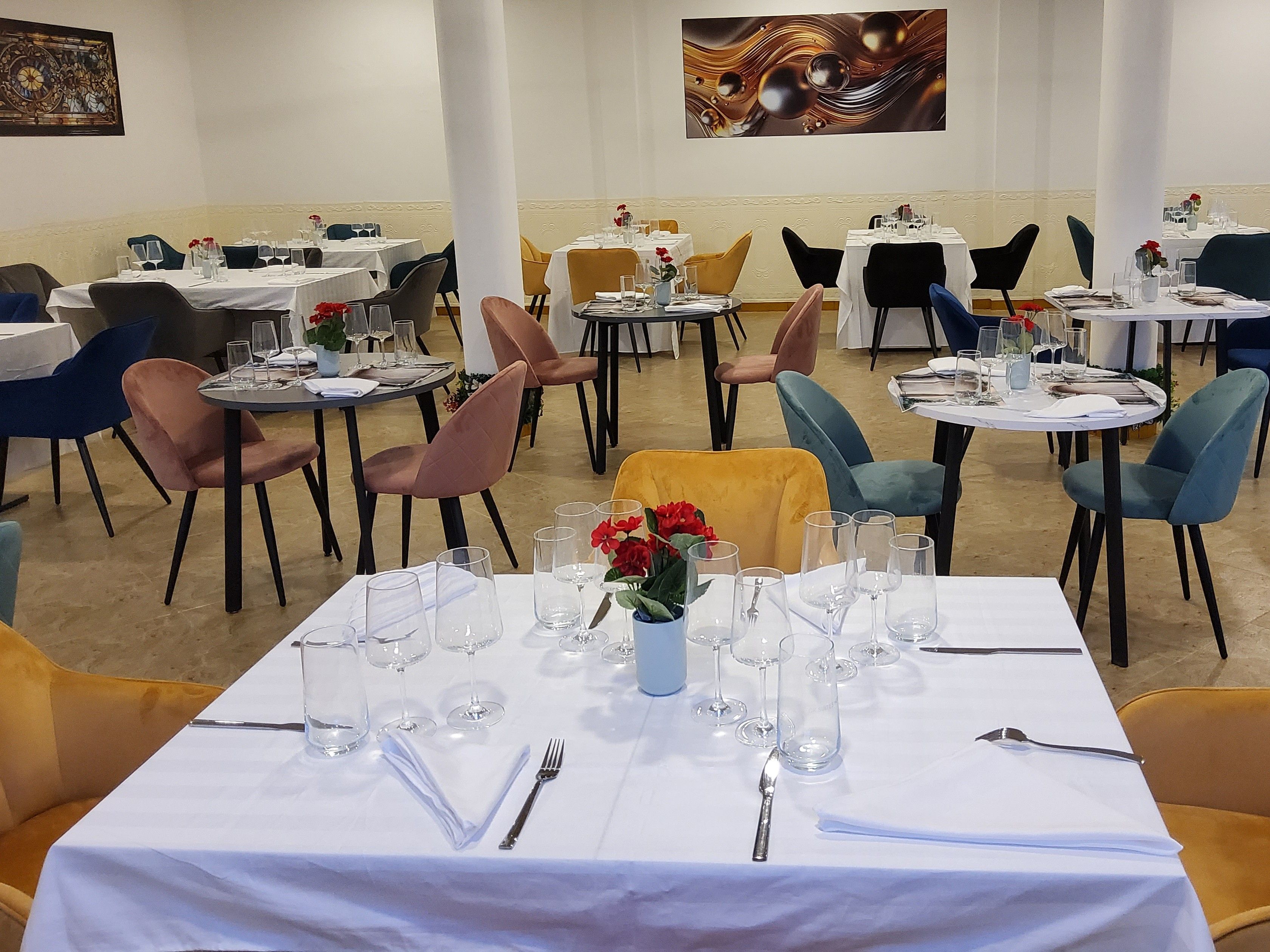 A restaurant with multiple tables set for dining, featuring a variety of chairs and a central floral arrangement.