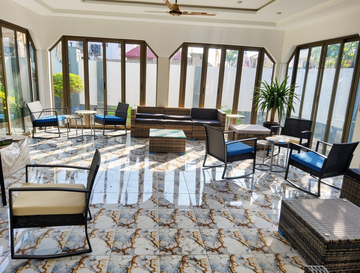 A sunlit room with a sofa, chairs, and a table, large windows, and a ceiling fan.