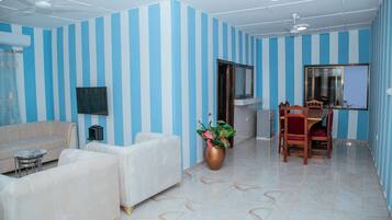 Una sala de estar con paredes a rayas, un sofá, un televisor, una zona de comedor con sillas y una planta grande.