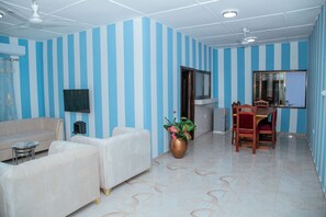 Una sala de estar con paredes a rayas, un sofá, un televisor, una zona de comedor con sillas y una planta grande.