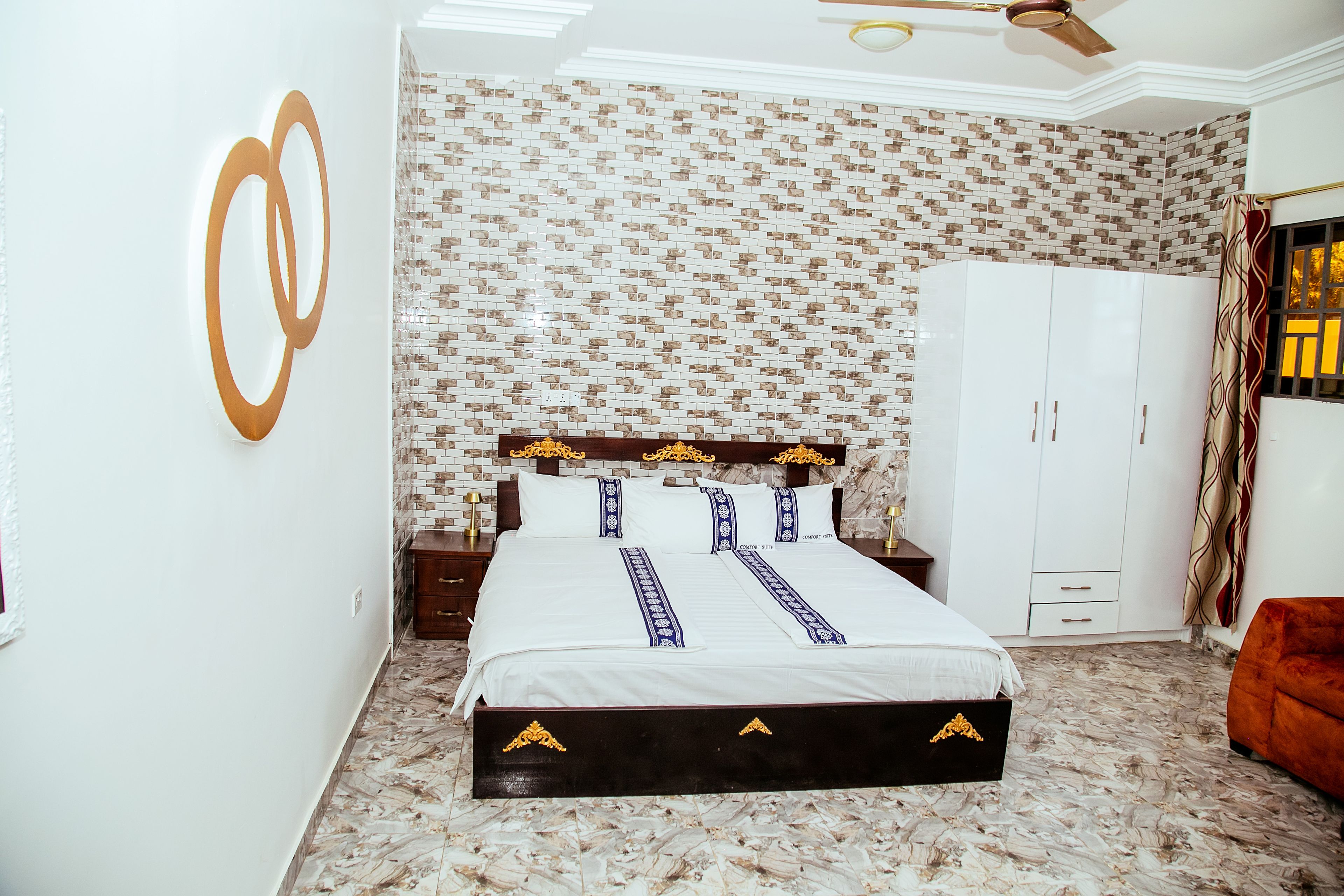A hotel room with a bed, a wardrobe, a nightstand, and a wall with a patterned design.