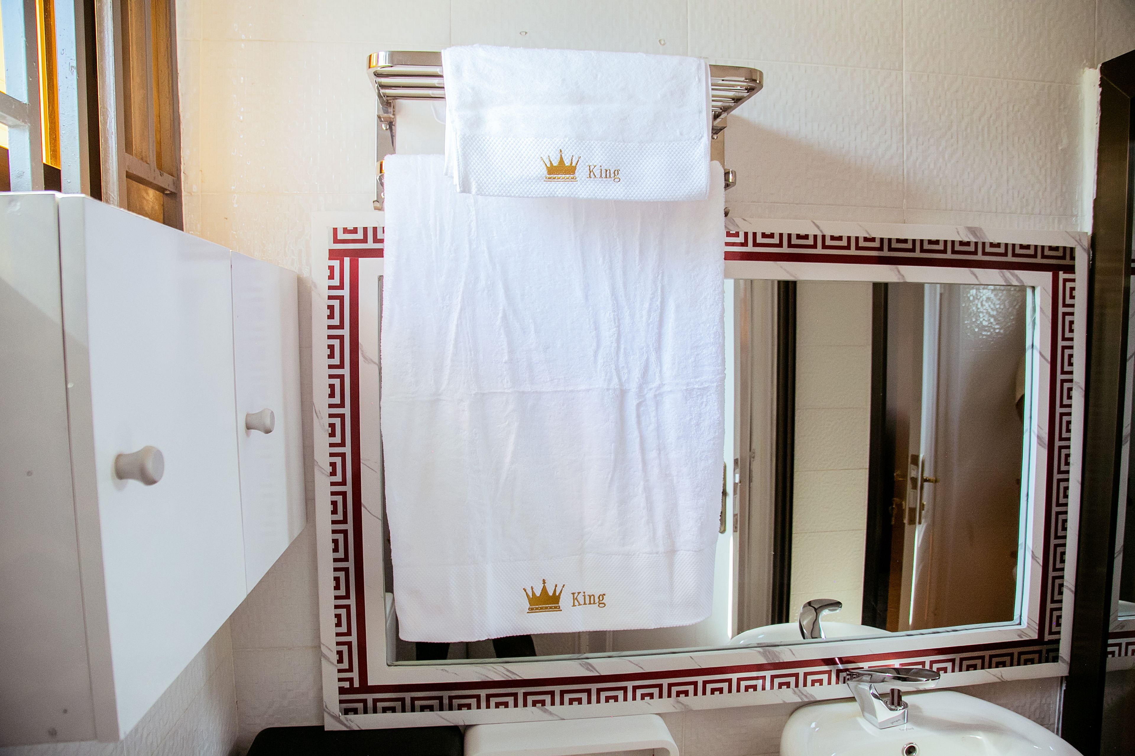 A bathroom with a white sink, a mirror with a decorative frame, and a towel with a crown and the word "King" on it.