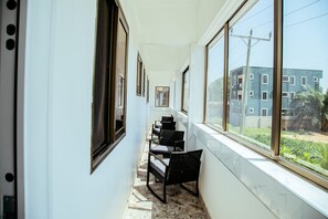 A corridor with a row of chairs and tables, large windows, and a view of a building outside. - CK Suites (Adentan)