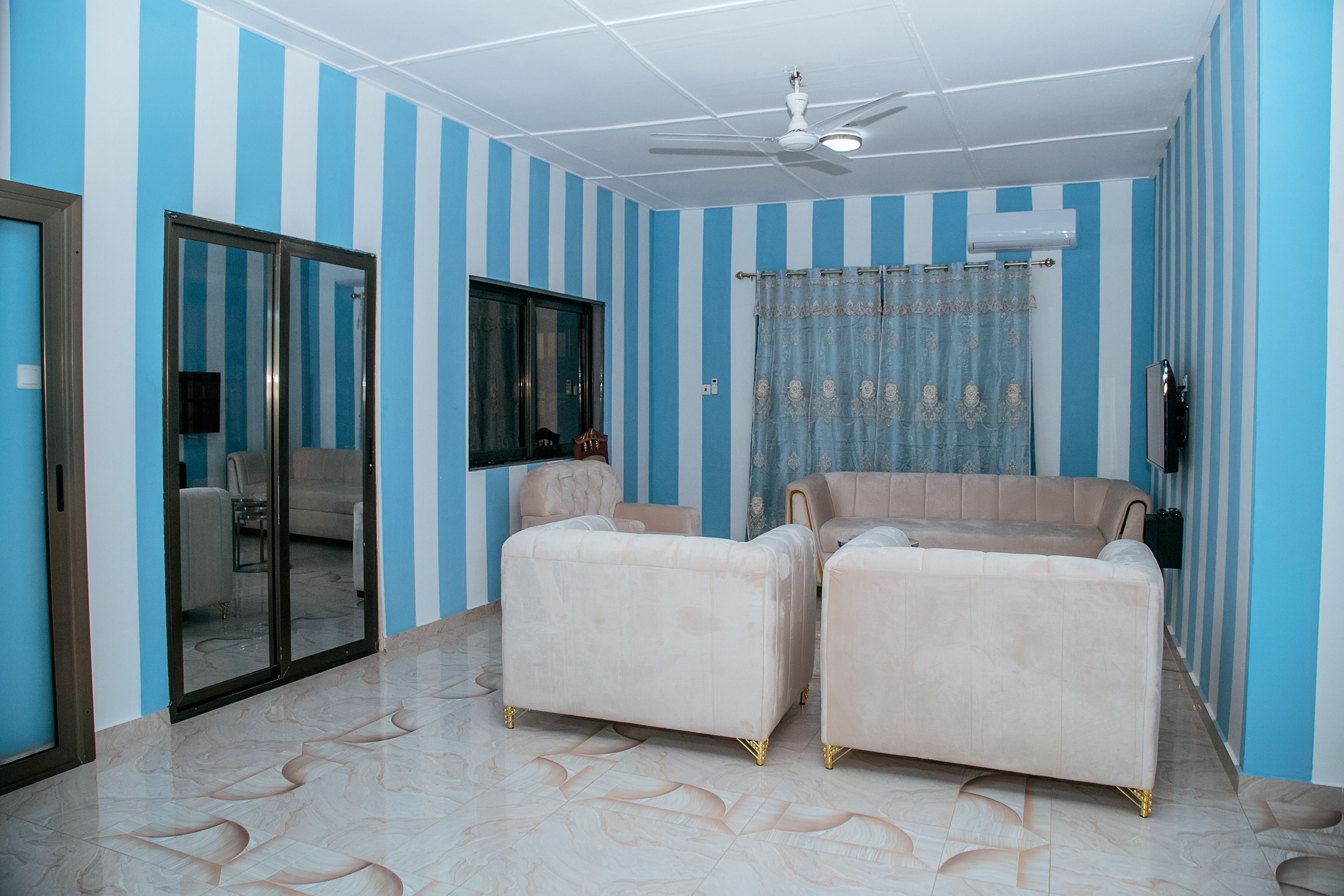 Una habitación con paredes a rayas, ventilador de techo, un sofá y una silla.