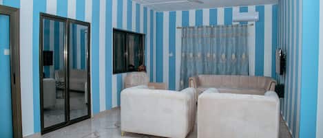 Une pièce aux murs rayés, avec un ventilateur de plafond, un canapé et un fauteuil.