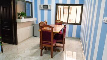 A dining area with a wooden table and chairs, a potted plant, a microwave, and a window with a view.