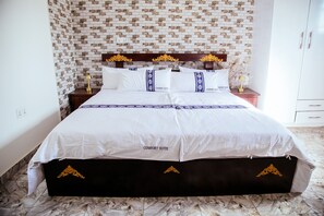 Una cama con colcha suave color blanco, cabecera de madera y suelo de mármol.