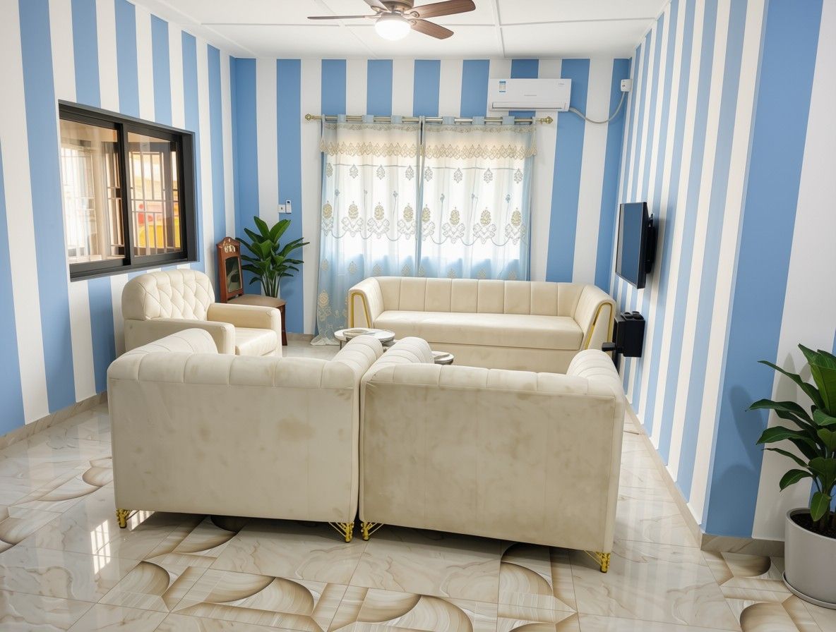 A living room with striped walls, a ceiling fan, a window with blinds, a sofa set, a television, and a potted plant.