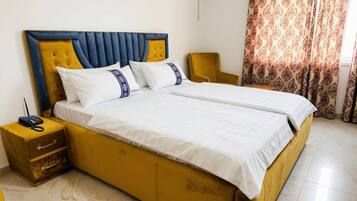 Un letto matrimoniale con testiera, un comodino con cassetti, una sedia e una tenda decorata.