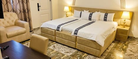 A hotel room with a large bed, two bedside tables, a desk, a chair, and a patterned floor.